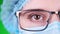 Green background. close-up, eye, part of female doctor face in glasses, in blue medical mask and medical cap.