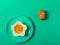 Green background with egg in a flower shaped bowl and green plate with broken egg shells and kitchen utensils