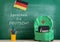 green backpack, blackboard with text "Sprechen Sie Deutsch?", flag of the Germany, school supplies and notebooks