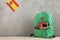 Green backpack, flag of the Spain and school supplies, smartphone and headphones against a cement wall