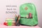 Green backpack, text & x22;Welcome back to school& x22; and school supplies: notepad, books, scissors, calculator