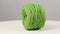 Green ball of cotton yarn spinning on a white background.