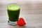 Green barley juice drink in glass and red heart on wood background.