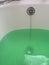 Green bath water in white enamel bath with chrome plug.