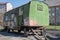 Green, battered metal trailer on wheels with closed windows and traces of graffitit, standing in a apartment buildings courtyard