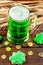 Green beer in a glass mug with gingerbread clover, horseshoe, wheat spike and gold coins on a rustic wooden surface. Festive