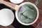 Green bentonite clay in the bowl, cotton pads and cosmetic brush. Clay texture close up. Diy mask and body wrap recipe.