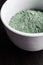 Green bentonite clay powder in the white bowl. Clay texture close up. Diy facial mask and body wrap recipe.
