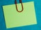 green blank note pinned to a blue notice board with a paper clip