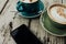 Green and blue cup coffee and smartphone rests on a wooden table