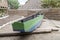 Green and blue wooden boat with oars, next to a path