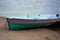 Green boat with stripes on the shore behind water.