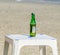 Green bottle of beer standing on a white beach table, close up
