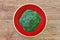 Green broccoli inflorescence on a bright red plate on a wooden tabletop