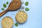 Green buckwheat, sprouted buckwheat in wooden bowls brown buckwheat grains in wooden spoon with green leaves on blue background.