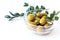 Green canned olives in a glass cup with myrtle branches on a white background, close-up