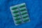 Green capsules of tablets in a gray blister on blue matter