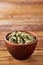 Green cardamon in ceramic bowl on rustic wooden background close-up, top view, selective focus, vertical.