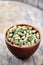 Green cardamon in ceramic bowl on vintage wooden background close-up, top view, selective focus, vertical.