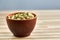 Green cardamon in ceramic bowl on wooden table close-up, top view, selective focus.