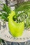 Green ceramics statuette..of rooster and green plants in white pots on garden table. Beautiful garden arrangement