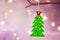 Green Christmas tree with red star ornament hanging on branch. Shining garland golden lights. Purple background.