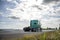 Green classic big rig semi truck tractor driving on the road with cloudy sky to warehouse for pick up the loaded trailer