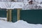 Green closed gate and part of the fence of metal and brick on the street in white snow