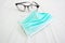 Green color Surgical Mask and round shaped black eye glasses on the patient bed sheet - image