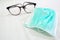Green color Surgical Mask and round shaped black eye glasses on the patient bed sheet - image