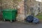 Green container and pile of garbage bags. Lots black garbage bag with street and old brick wall background
