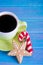 Green cup of hot coffee with glazed festive Christmas cookie on blue wooden background.