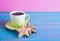 Green cup of hot coffee with glazed festive Christmas cookie on blue wooden table.