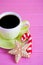 Green cup of hot coffee with glazed festive Christmas cookie on pink wooden background.