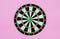 Green dart arrow hitting in the target center of dartboard, metaphor to target success, winner concept, on pink pastel background