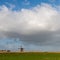 Green dike with windmill, blue winter sky and coulds