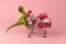 green dinosaur toy with shopping cart full of present boxes on a soft pink background