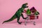 green dinosaur toy with shopping cart full of present boxes on a soft pink background