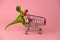 green dinosaur toy with shopping cart on a soft pink background