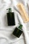 Green dispenser bottles of shampoo and shower gel, wooden comb on white towel in bathroom