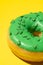 Green donut on a yellow background from the side, vertical photo. Studio shooting