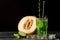 A green drink with lime and tarragon. A cocktail and a melon on a black background. Healthy, sweet and tasty drinks. Copy space.