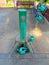 Green drinking park fountain with set of four green plastic watering cans and wooden benches bottom for sitting