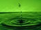 A green drop drips into the water and creates splashes of various shapes