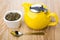 Green dry tea in glass bowl, yellow teapot and teaspoon