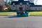 Green dumpster bag full of black plastic garbage bags on an asphalt street near the curb in front of a large house with a big