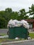 A green dumpster overflowing with full plastic trash bags