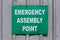 Green Emergency Assembly Point sign mounted to a metal fence.