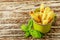 Green enameled cup with potato fries decorated with basil leaves, over wooden table. Side view.