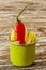 Green enameled cup with potato fries decorated with a red chilly pepper, over wooden table. Vertical. Side view.